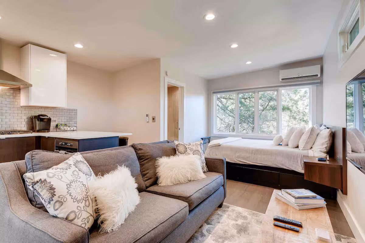 Open-concept interior of The Cabin with sofa seating, modern kitchen, and sleeping area overlooking wooded views
