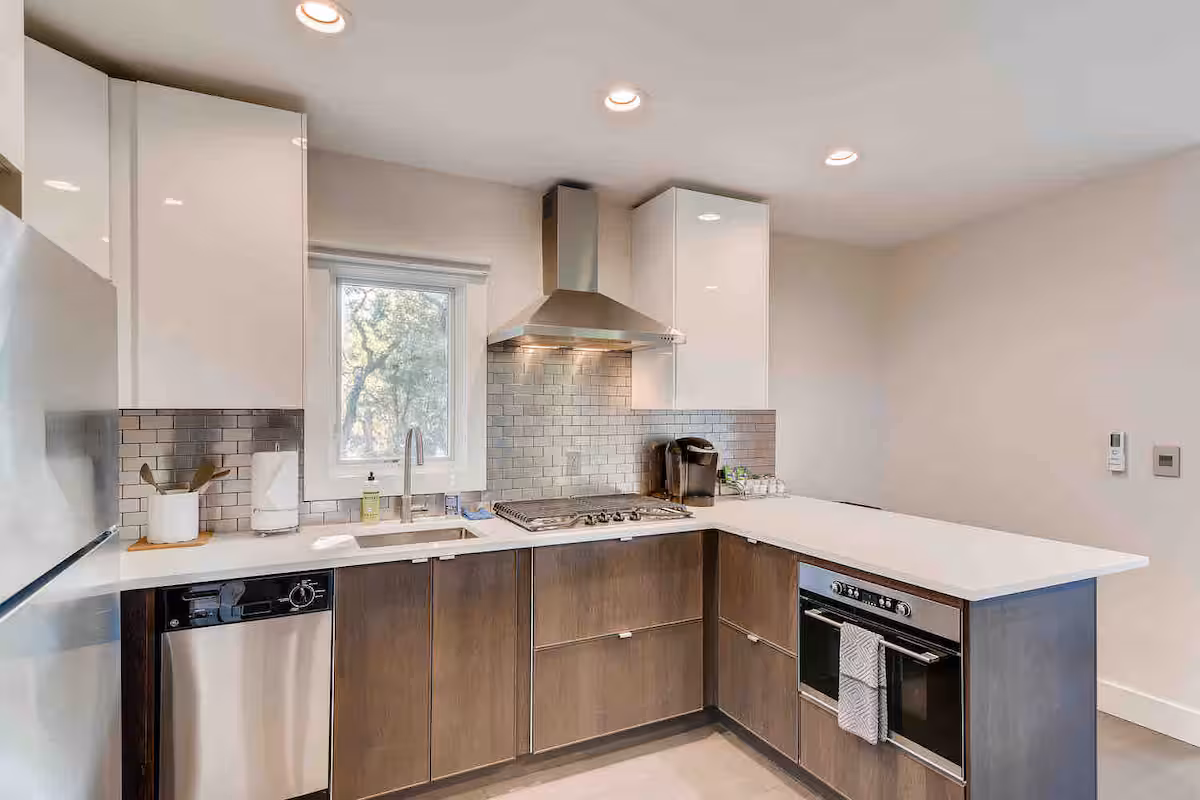 Modern kitchen inside The Cabin, featuring sleek white cabinetry, warm wood lower cabinets, stainless steel appliances, quartz countertops, and a clean tile backsplash, bright, functional, and thoughtfully designed for comfortable stays.
