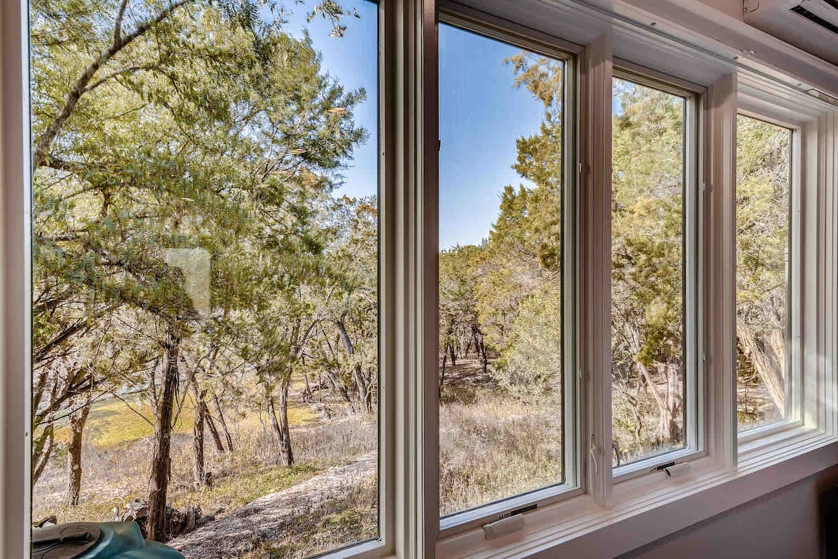 Interior view from The Cabin at Eco Valley looking out through large windows onto a peaceful wooded landscape, filling the space with natural light and forest views