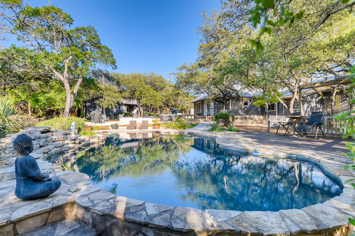 Natural stone swimming pool near The Cabin at Eco Valley featuring calm blue water, a seated Buddha statue, stone edging, lounge chairs, and cabins surrounded by trees in a peaceful retreat setting