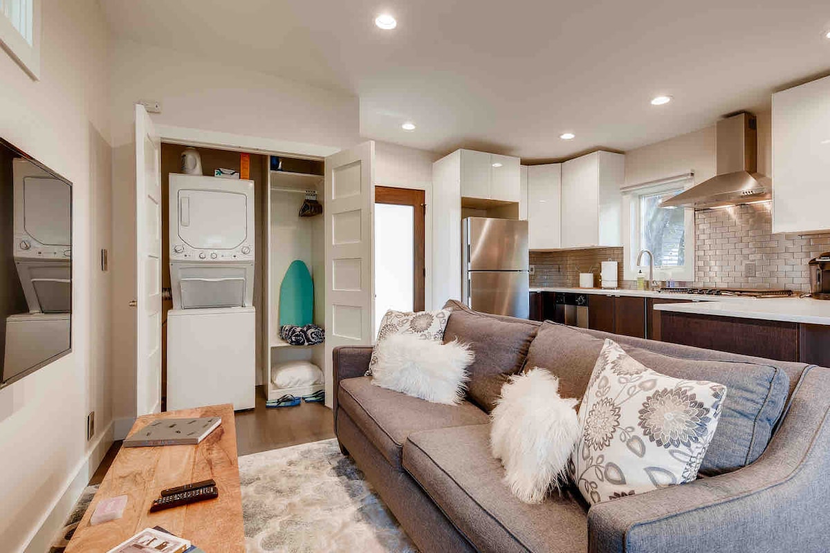 Open living area in The Cabin with sofa seating, washer and dryer, and modern kitchen in the background