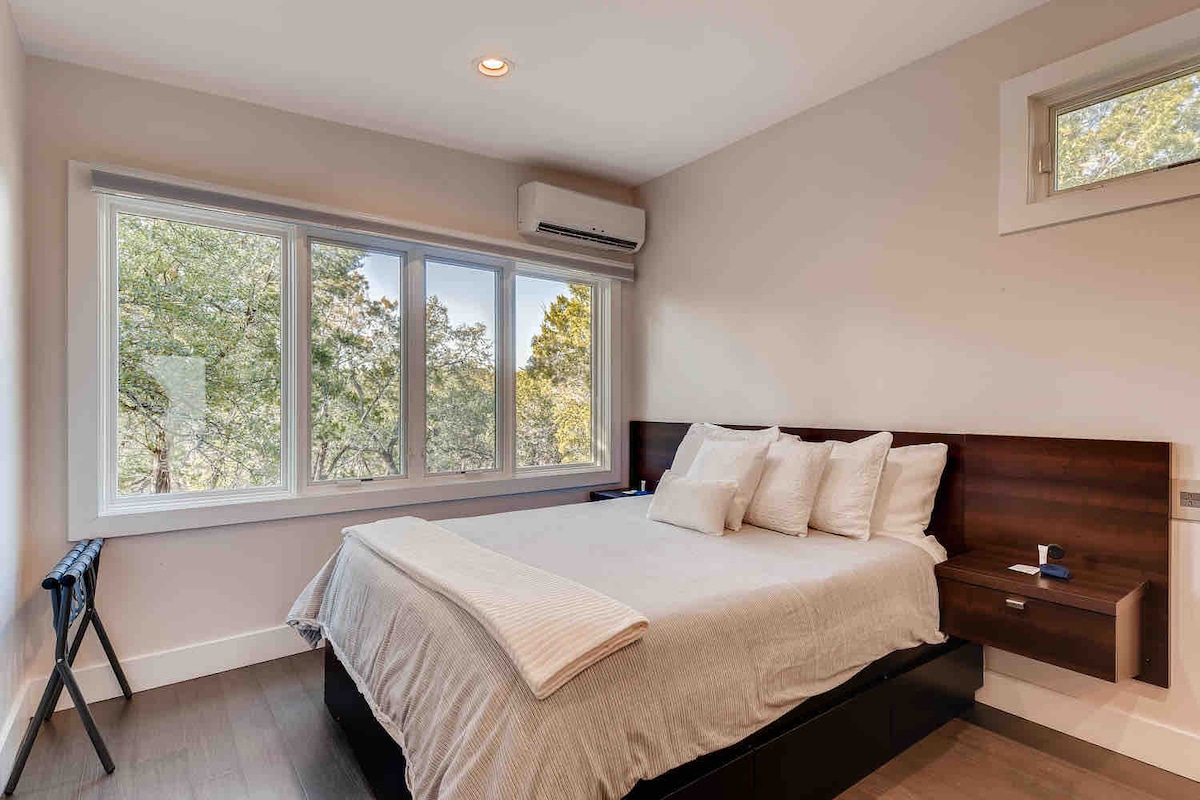 Cabin bedroom featuring a queen bed, large picture window, and peaceful views of the surrounding trees