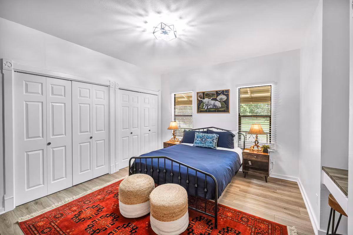 Casa Blanco bedroom with black metal bed, blue bedding, and red rug.
