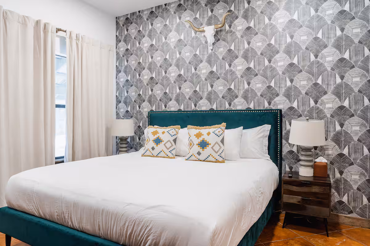Cowboy Apartment bedroom with a green upholstered bed and patterned accent wall.