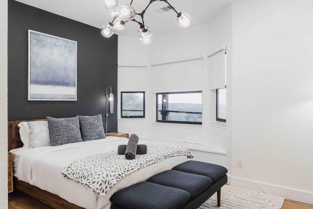 Bright bedroom at The Villa with a modern bed, black accent wall, and large windows overlooking the landscape.