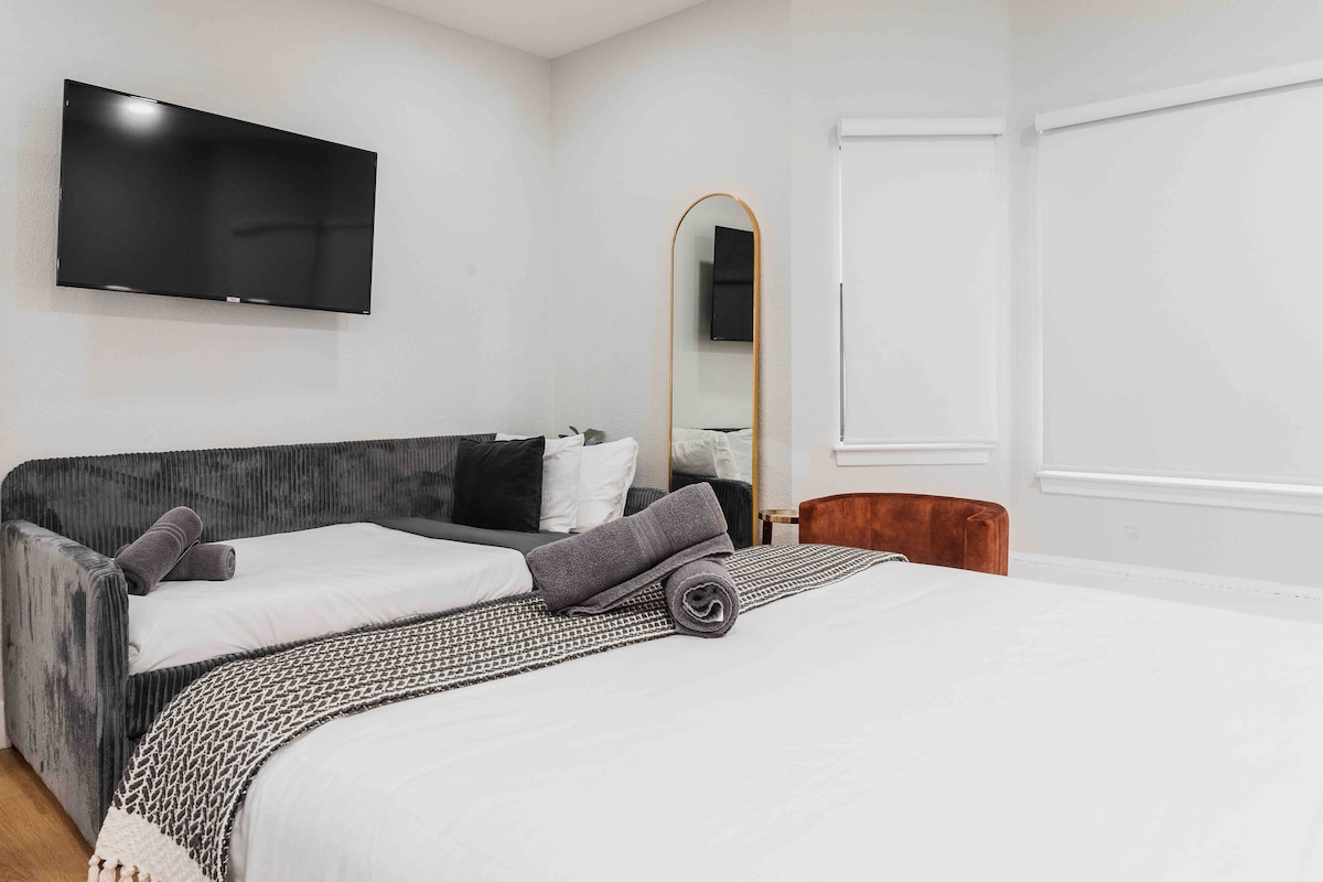 Bedroom in The Villa with king bed, additional sofa bed, wall-mounted TV, full-length mirror, and bright minimalist design