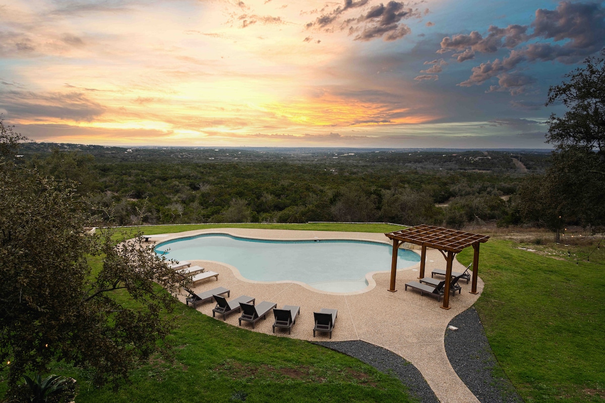 Hilltop pool at The Villa with lounge chairs, pergola seating, and panoramic sunset views over the landscape