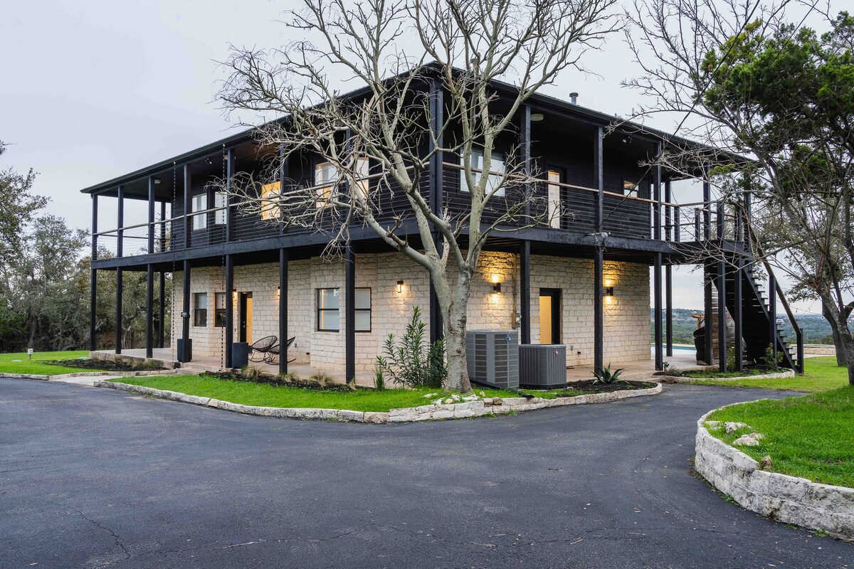Two-story exterior of The Villa with wraparound balcony, stone façade, and surrounding trees