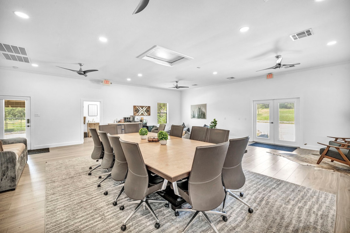 Wide meeting space at High Tech Hacienda with large conference table, rolling chairs, ceiling fans, and natural light.