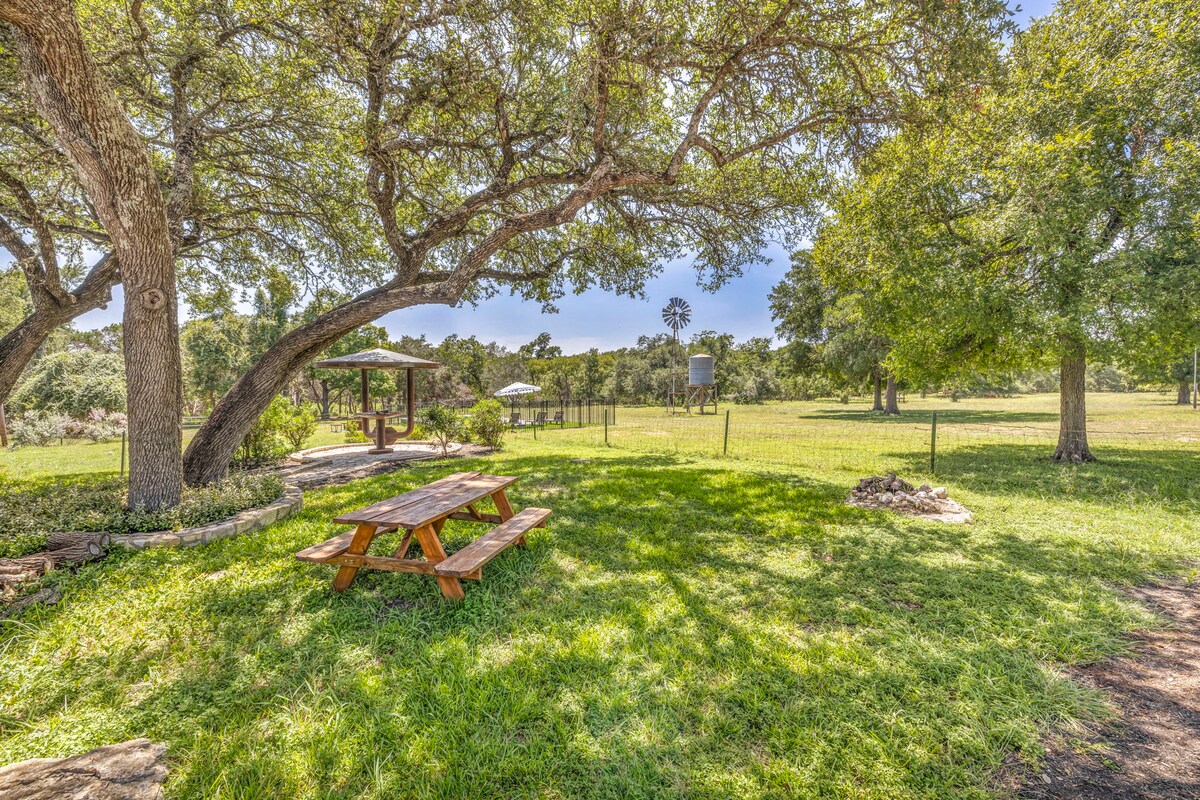 Shaded picnic area at High Tech Hacienda with wooden table, mature trees, and open grassy fields.