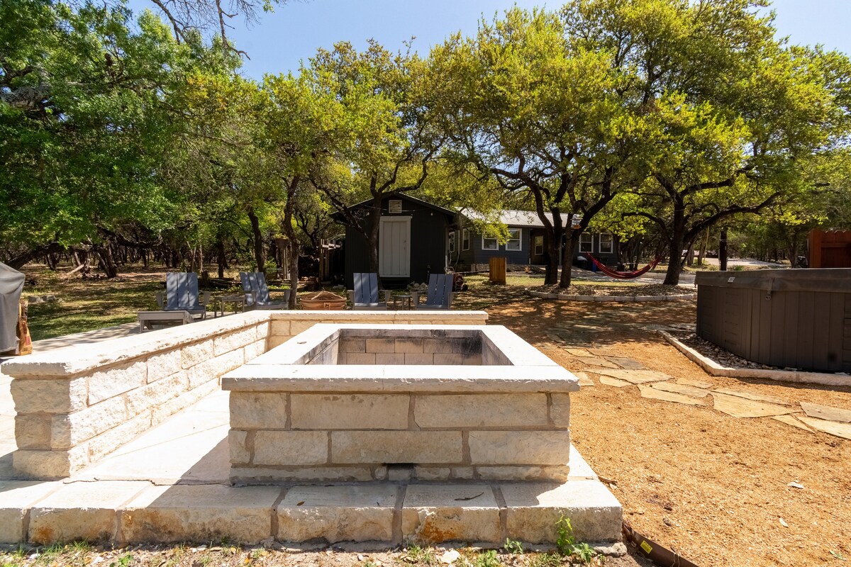 Stone fire pit gathering area at The Nook at Eco Valley with built-in seating, Adirondack chairs, and oak trees creating a relaxed outdoor communal space