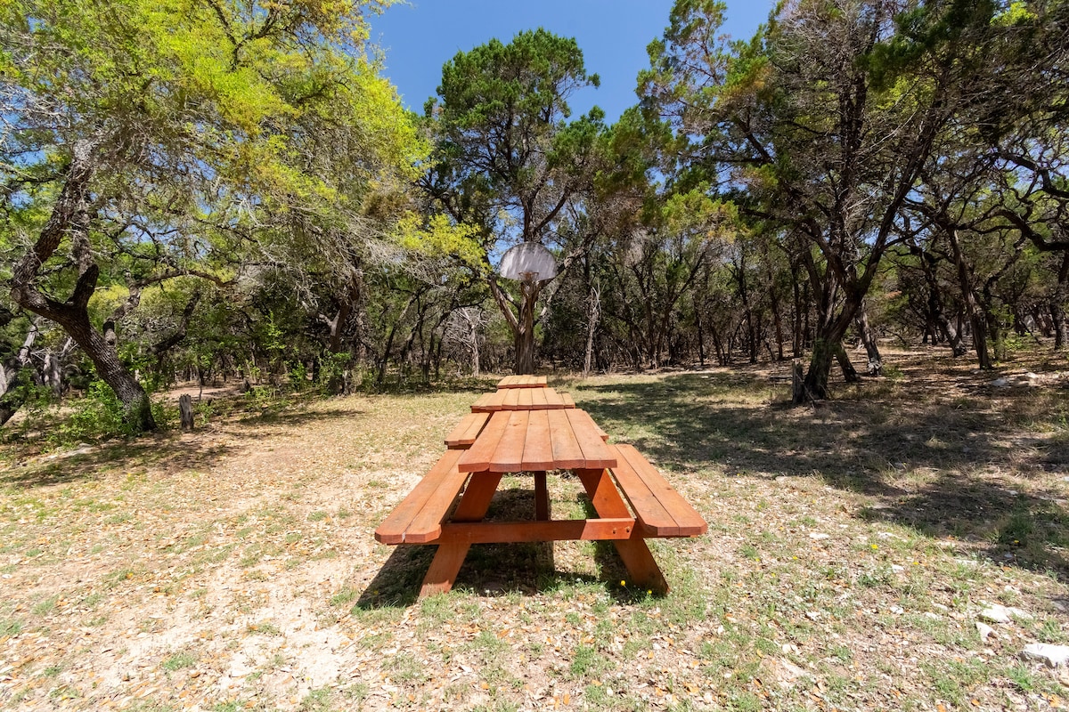 Wooden picnic table set in a shaded forest clearing at the Nook surrounded by native trees and natural ground cover