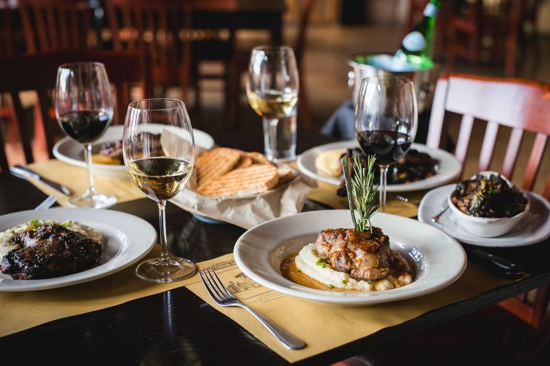 Plated Italian dishes and glasses of wine on a rustic dining table at Trattoria Lisina, featuring pasta, bread, and hearty entrées in a warm restaurant setting