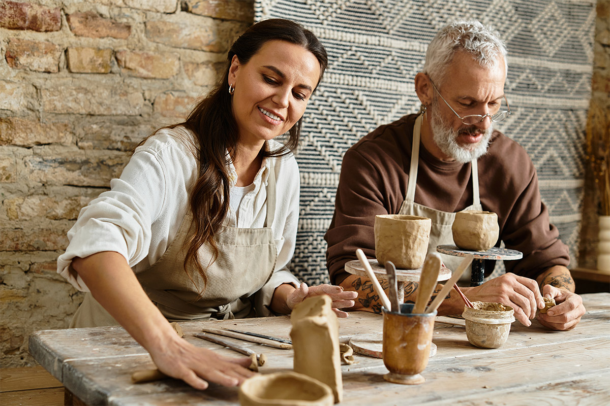 Two adults working together at a table shaping clay pottery during a hands-on workshop.