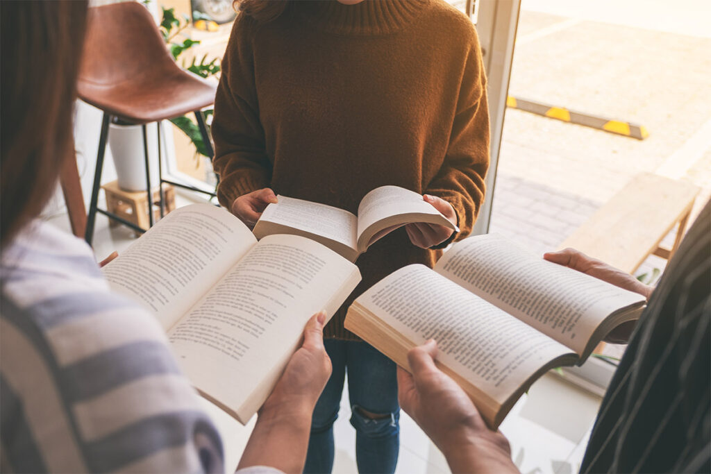 Small group of people standing together holding open books during a book club discussion.