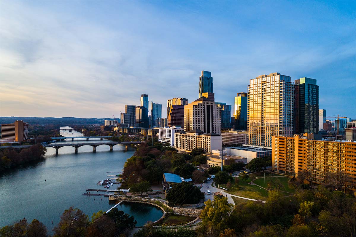 Downtown Austin skyline at sunset, with high-rise buildings overlooking Lady Bird Lake and the Congress Avenue Bridge.