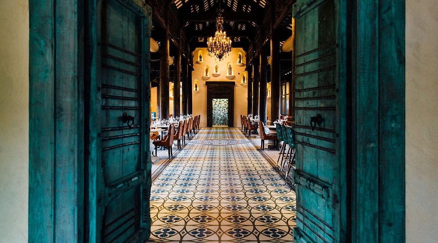 Interior of Tillie’s Culinary featuring open teal wooden doors, patterned tile floors, long dining tables, and chandeliers in a warm, elegant restaurant setting.