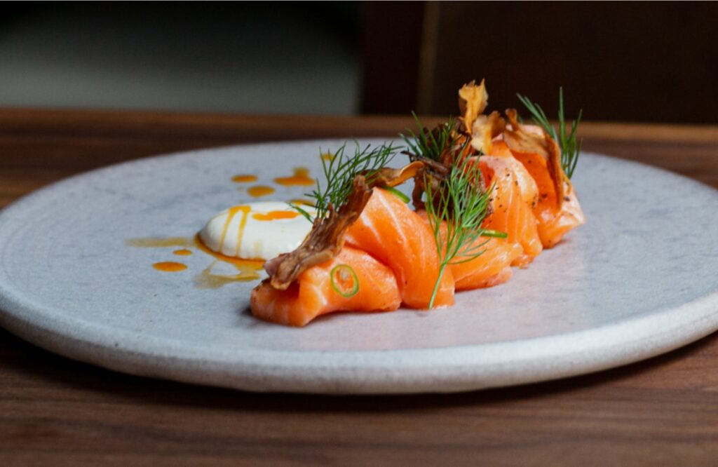 Uchi Sushi – Artfully plated salmon sushi topped with fresh dill and crispy garnish, served on a minimalist ceramic plate with sauce accents.
